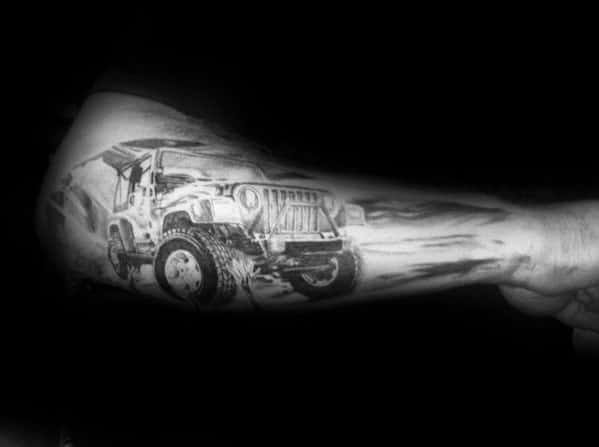 Realistic black and grey tattoo of an off-road Jeep in motion, featuring dynamic shading and dust effects for a rugged adventure look on the forearm.