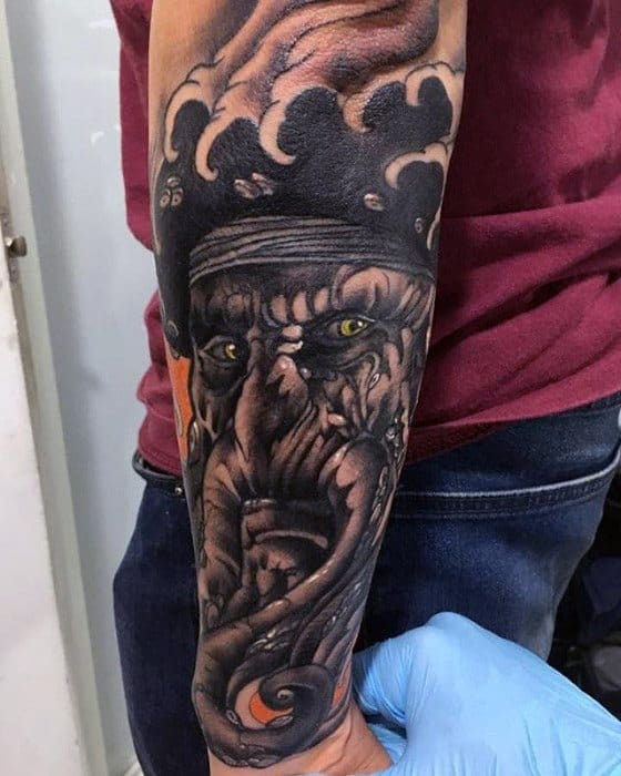 Forearm tattoo of Davy Jones' fierce face with glowing eyes and intricate patterns