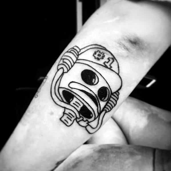 Black and white tattoo of SpongeBob's helmet character with a #1 cap and bold outlines, placed on the forearm.