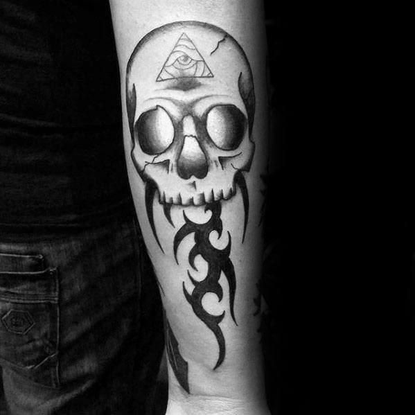 Forearm tattoo of a skull with glowing eyes, tribal flames below, and an all-seeing eye in a triangle on the forehead.