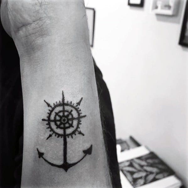 Anchor and ship wheel tattoo on the wrist with fine black details, symbolizing stability, direction, and a deep connection to the sea.