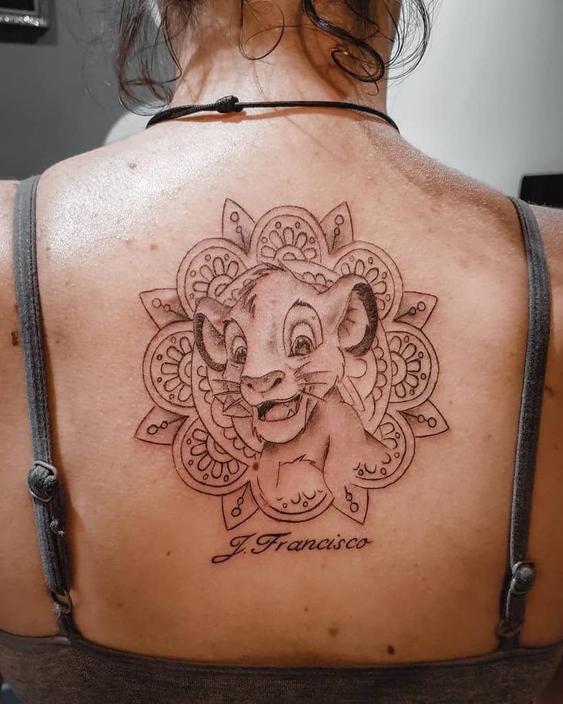 Delicate tattoo of Simba as a cub surrounded by intricate mandala patterns, with the name 'J. Francisco' below