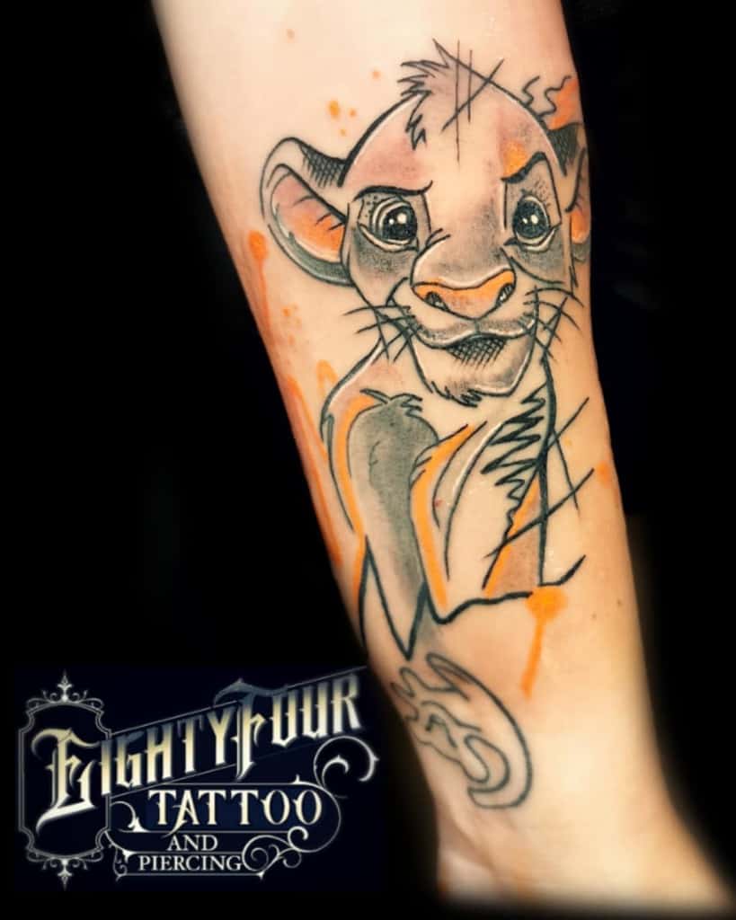 Stylized tattoo of Simba with detailed black linework and soft orange watercolor splashes