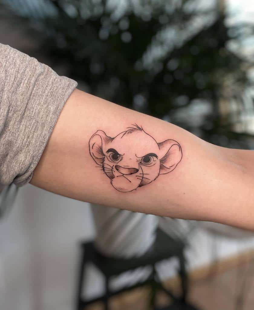 Simple and clean tattoo of Simba as a cub, capturing his determined and fierce expression in a minimalistic line style