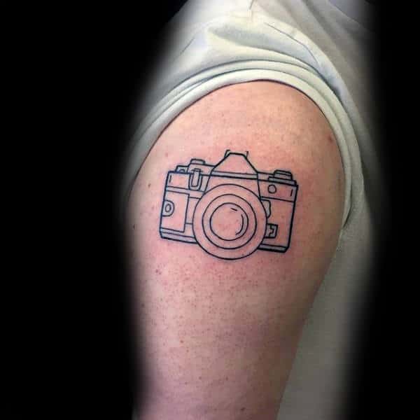 A minimalist line art design of a camera is inked on the upper arm, showcasing clean lines and intricate detailing that highlight the camera's classic features and contours