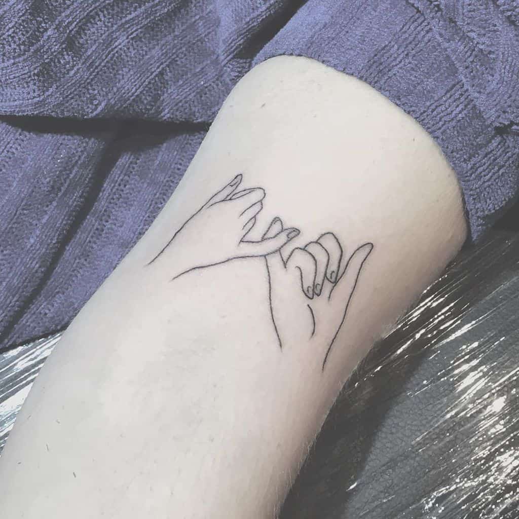 Tattoo of two hands making a pinky promise on an arm