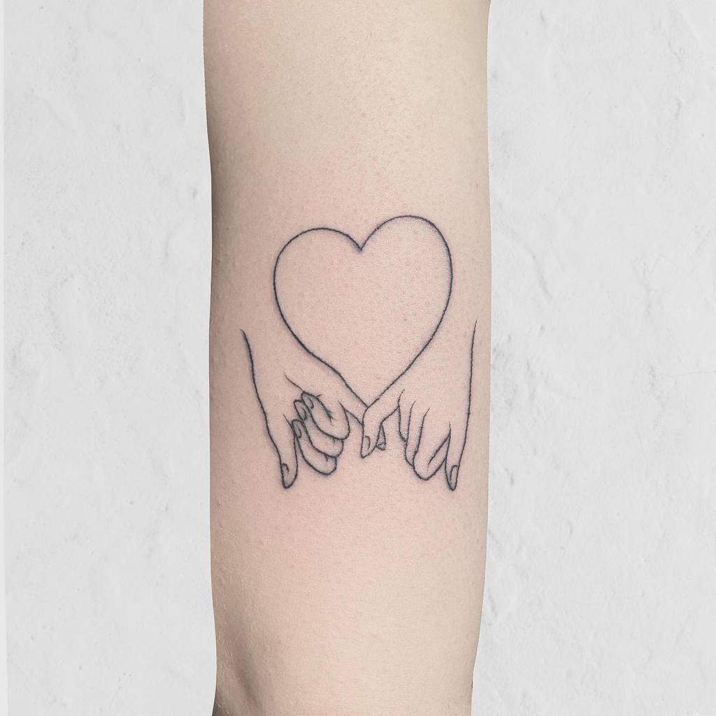 Line drawing tattoo of two hands making a pinky promise, forming a heart shape between them, on a  forearm