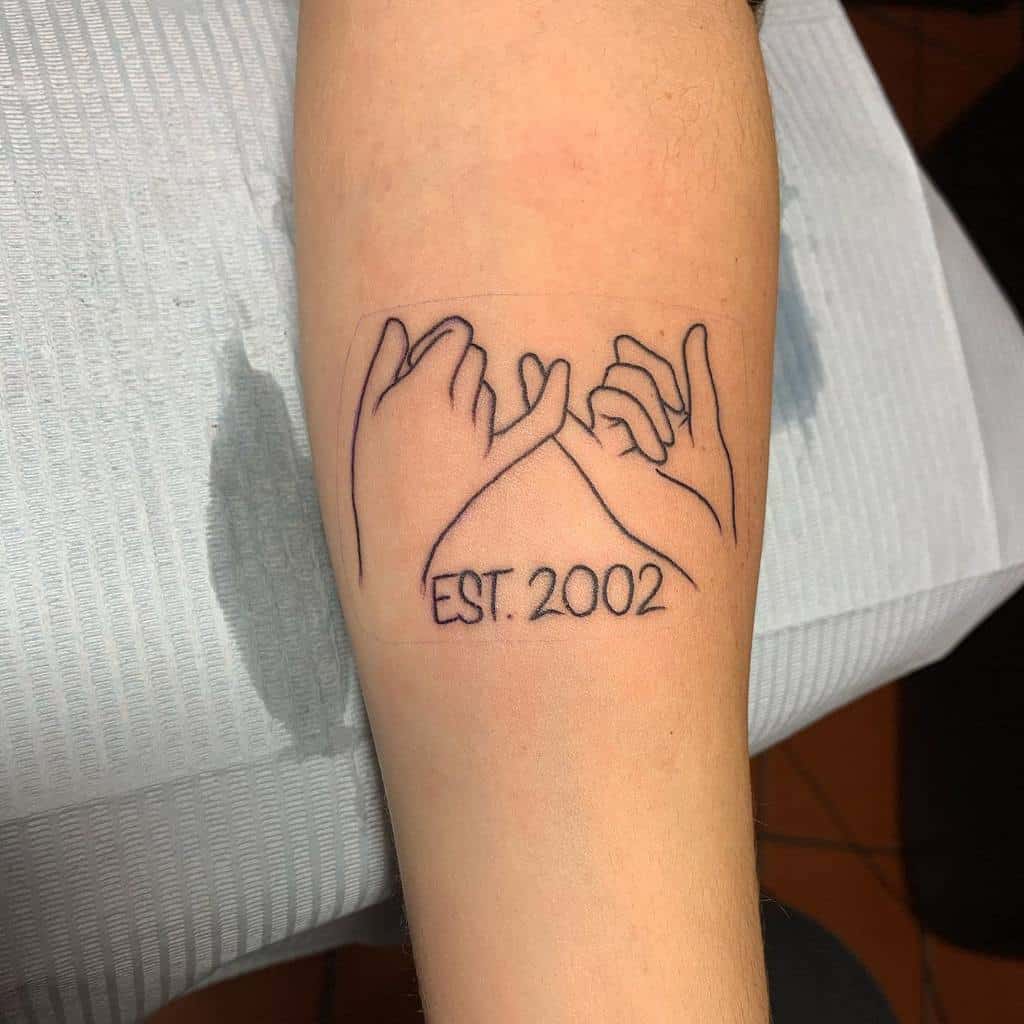 Tattoo of two hands making a pinky promise with "EST. 2002" written below on a forearm