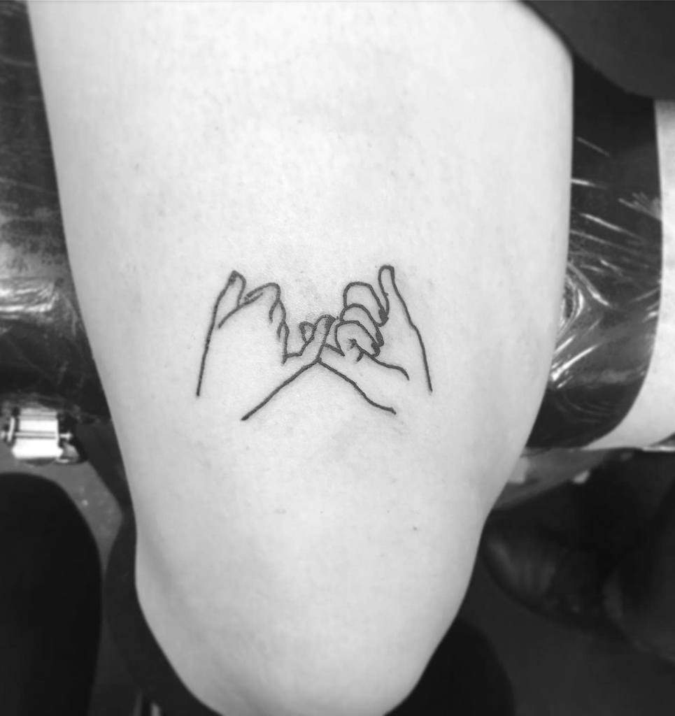 Minimalist tattoo of two hands making a pinky promise on a thigh in black ink