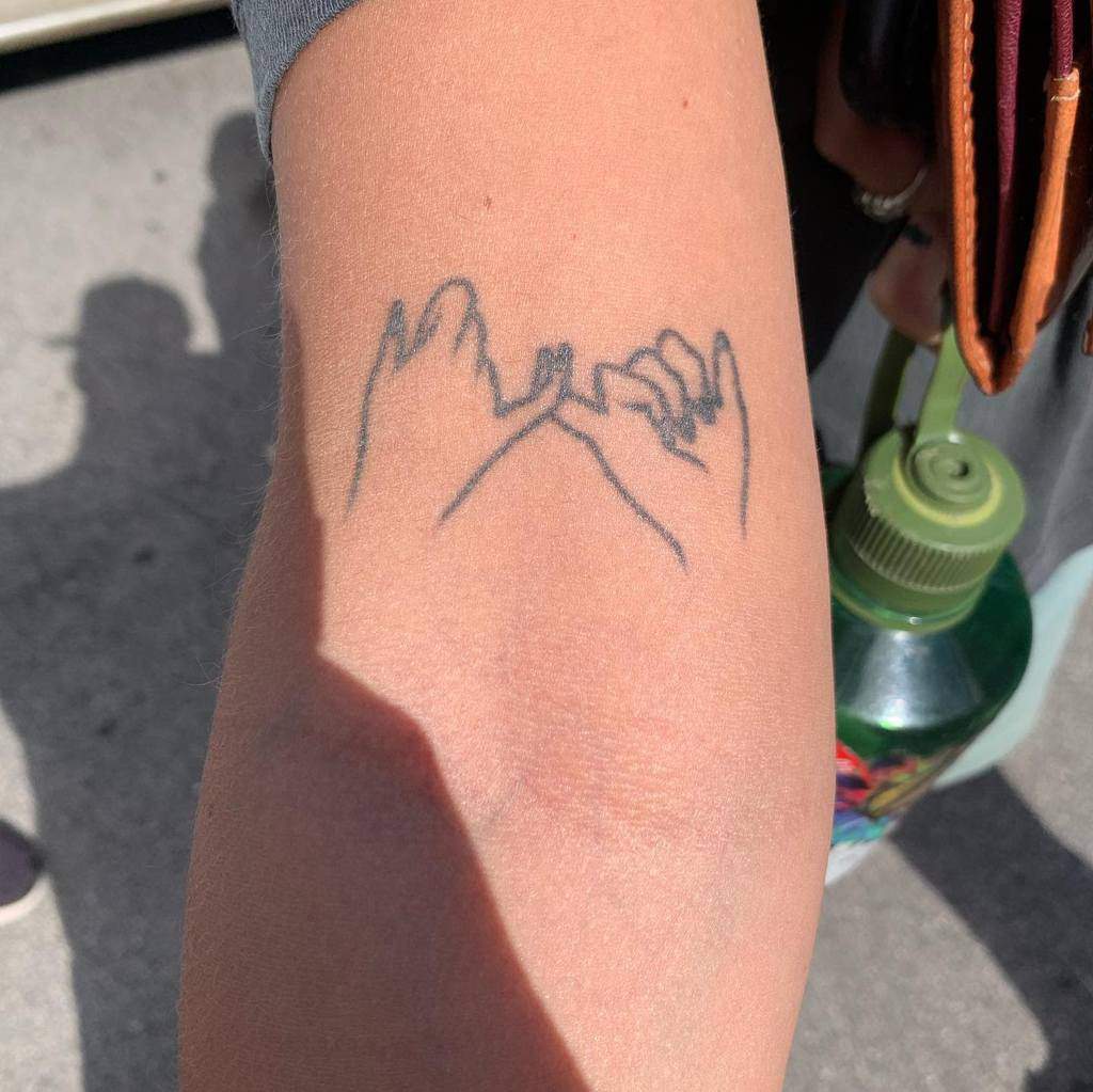 Minimalist pinky promise tattoo with fine line art on the forearm