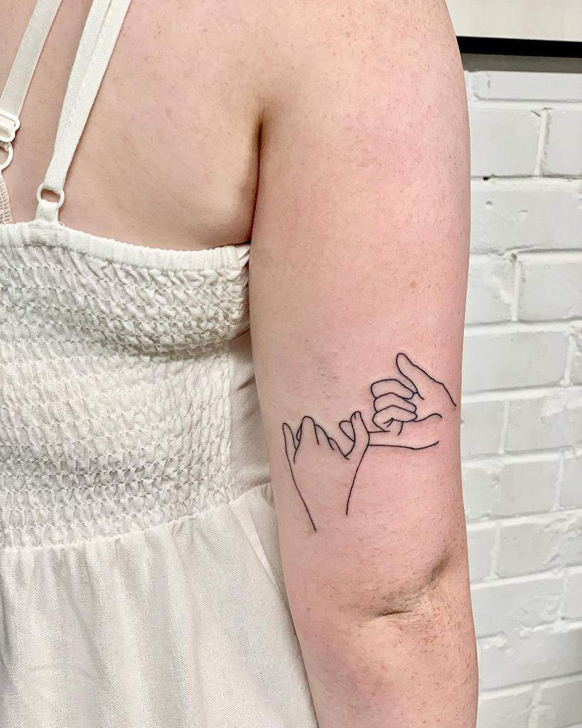 Line art tattoo of two hands making a pinky promise on a person's upper arm