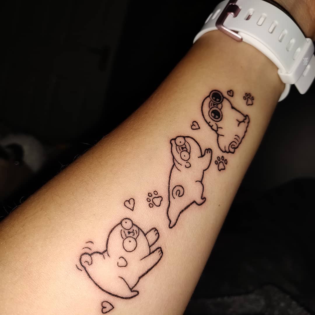 Tattoo featuring three playful, cartoonish pugs in different positions, with heart-shaped and paw print details around them
