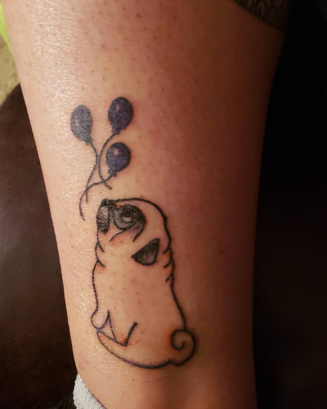 Black tattoo of a stylized sitting pug looking at three floating balloons 