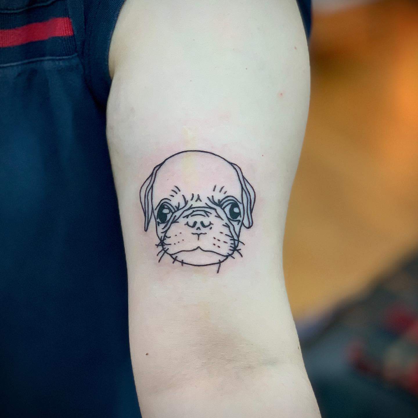 A simple, clean-line tattoo of a pug's face, highlighting its signature features such as the wrinkled forehead and expressive eyes