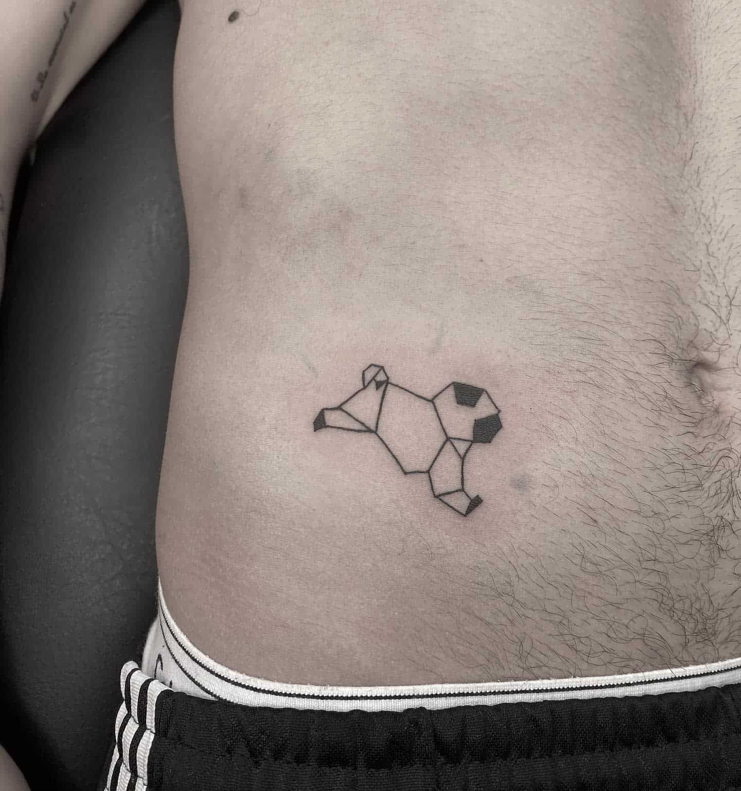 A geometric tattoo of a pug formed by various polygonal shapes and black lines, creating a minimalist and abstract design