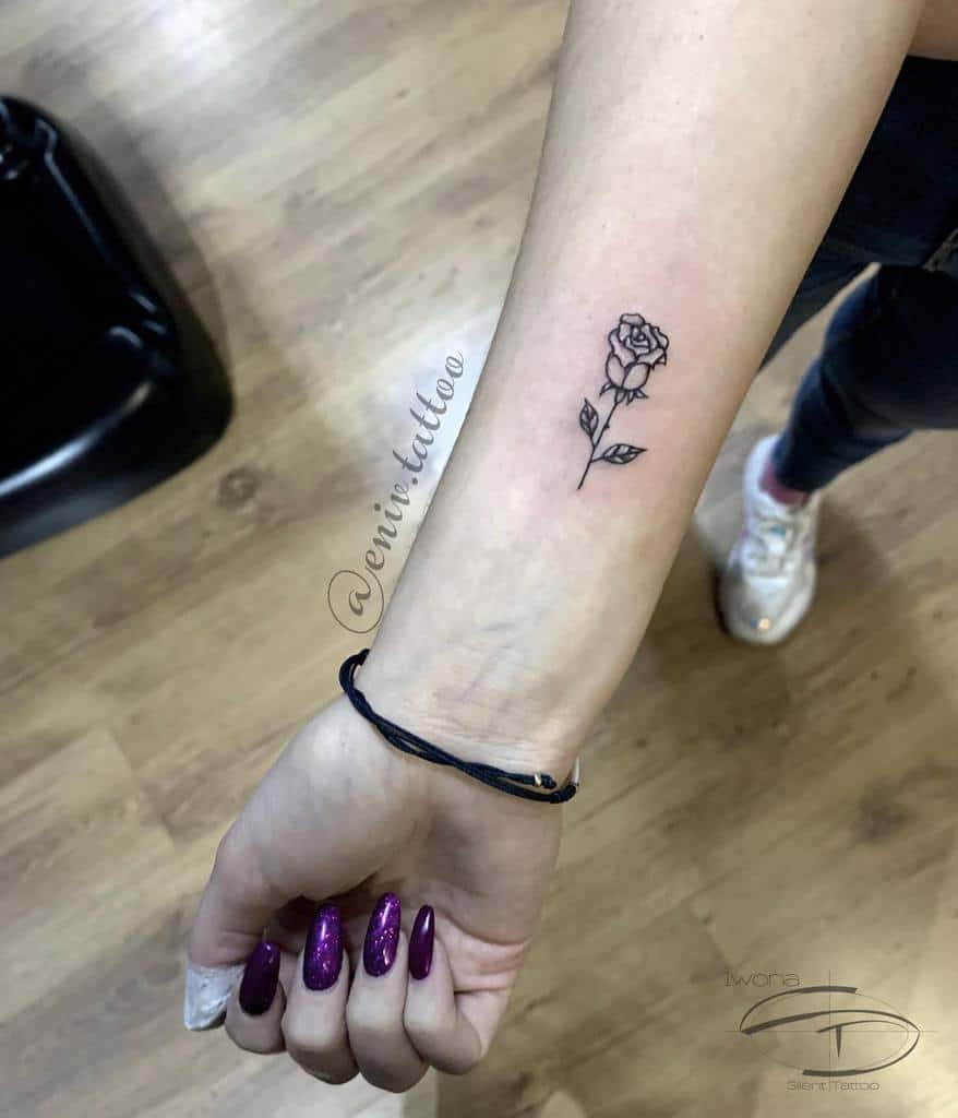 Forearm tattoo of a small, black rose on a forearm