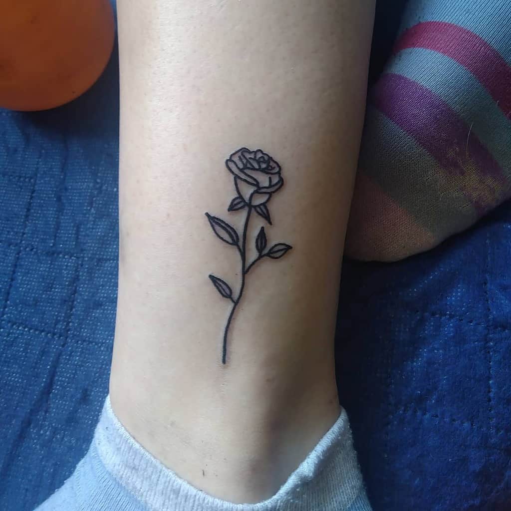 A black outline tattoo of a rose on a person's leg