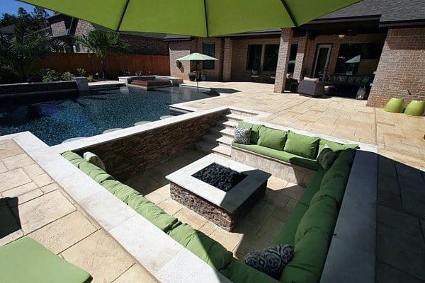 Modern outdoor patio with sunken seating encircling a cozy fire pit, beside a pool and under a large green umbrella
