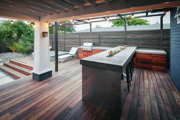 Modern outdoor kitchen bar featuring a cement countertop, wood decking, and an integrated grill.
