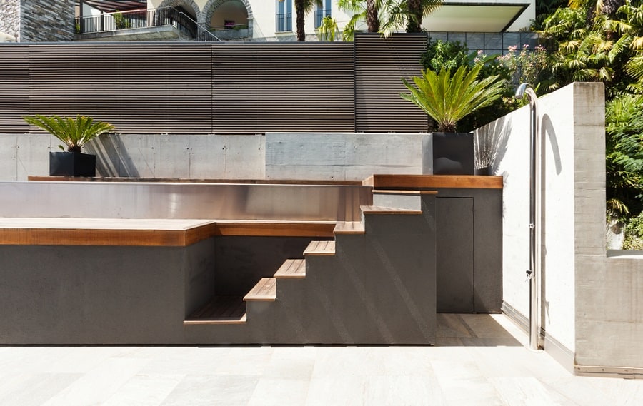 Modern outdoor shower next to a minimalist pool with wooden accents and tropical plants.