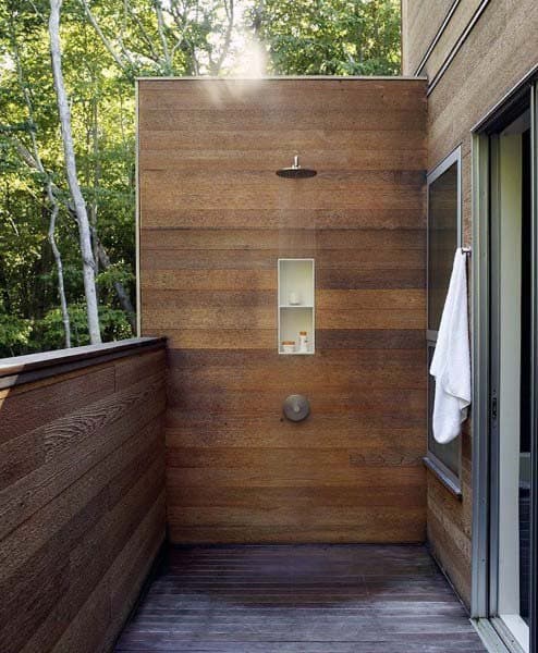 Rustic outdoor shower featuring a wooden panel wall, built-in shelf, and a seamless connection to nature.