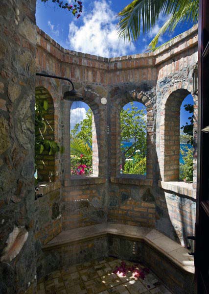 Rustic outdoor shower enclosed in a stone and brick structure with arched openings, offering scenic views and natural light.