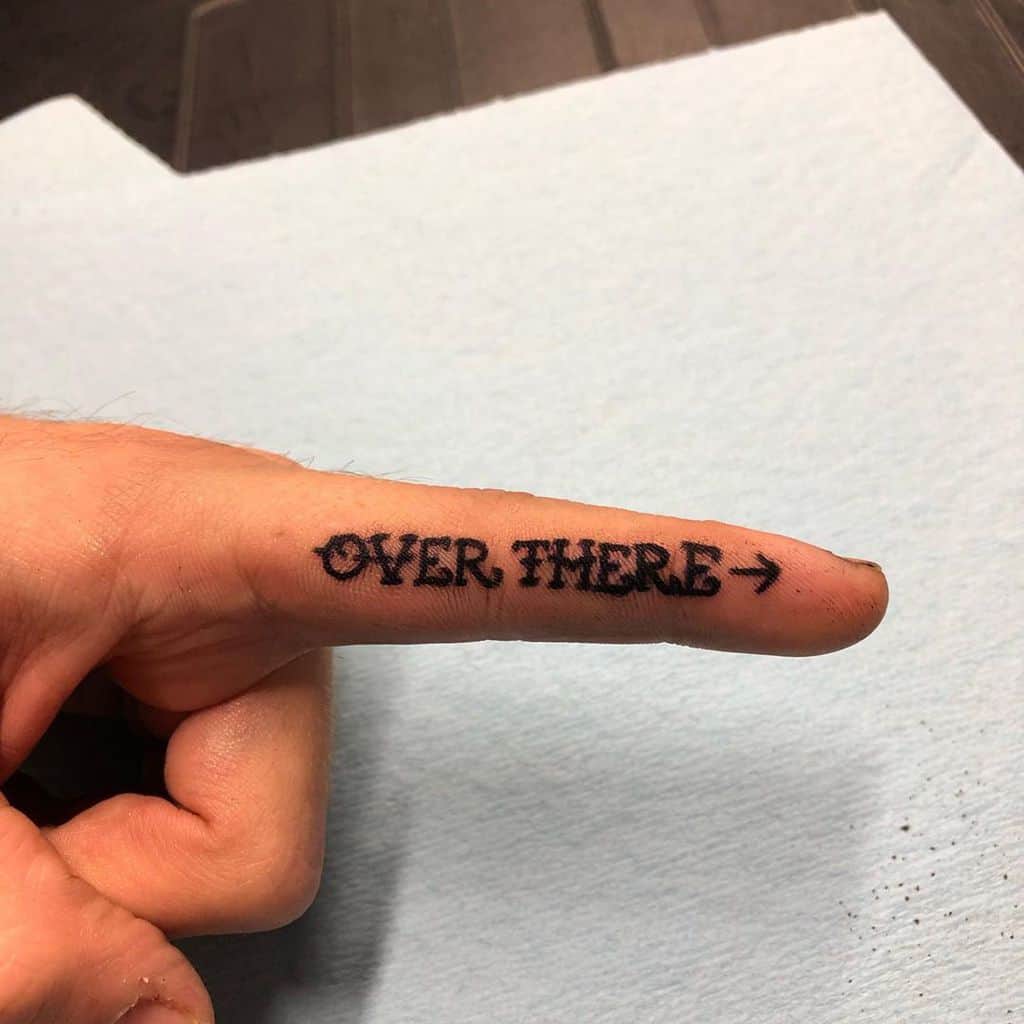 Funny tattoo on the index finger reading 'OVER THERE →,' turning a simple gesture into a permanent, witty pointing joke.