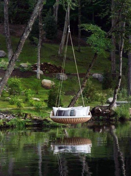 Round hanging daybed with cushions suspended over a tranquil forest pond.
