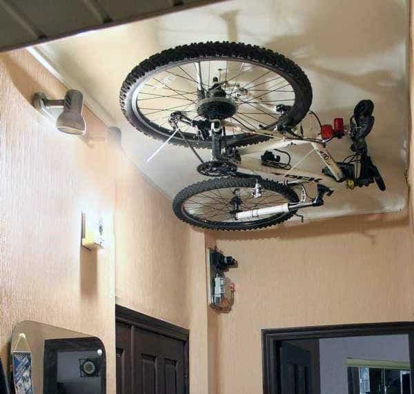 Two bicycles stored on a ceiling-mounted rack in a narrow indoor hallway.