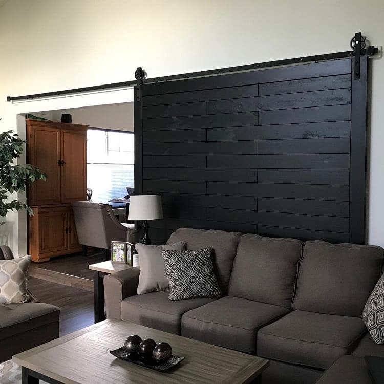 Black oversized sliding barn door behind a gray sofa in a modern living room setup.