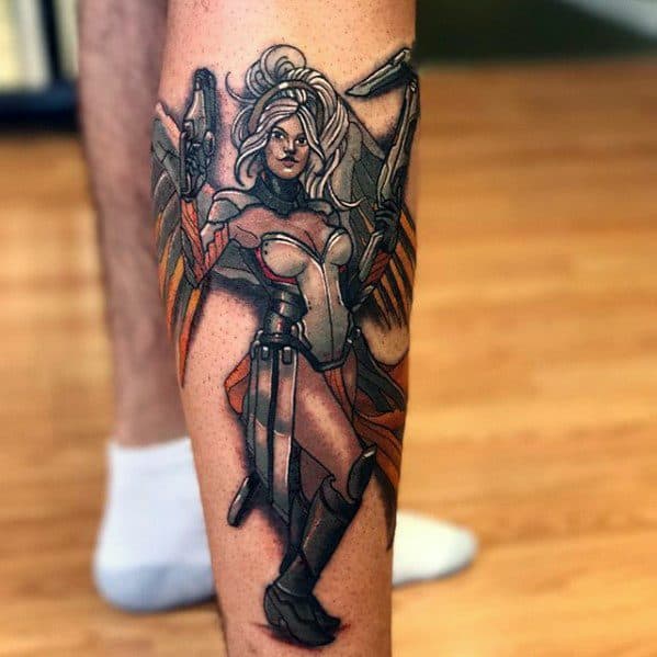 Colorful calf tattoo of Mercy from Overwatch, shown in a strong stance with her wings spread and staff in hand.