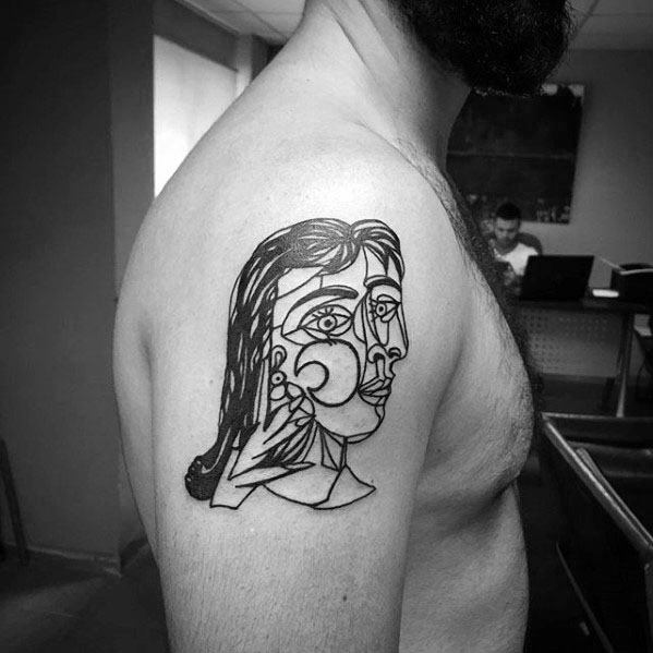Upper arm tattoo of a Picasso-style portrait with sharp lines, abstract features, and a contemplative expression in black ink.