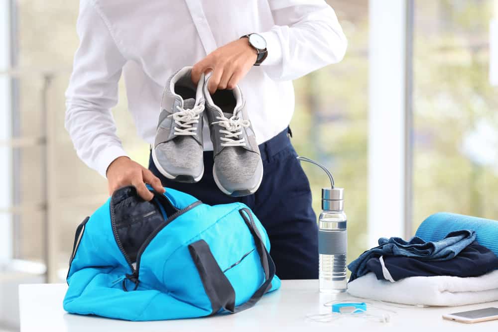 young businessman packing sports stuff into bag for training