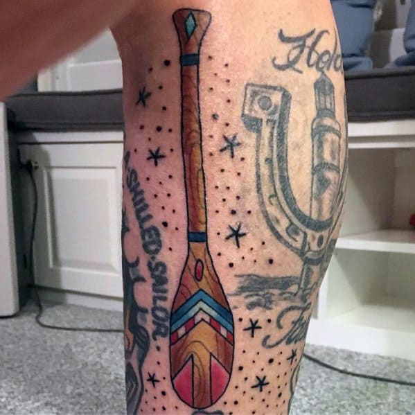 Colorful paddle tattoo with geometric patterns and bold outlines, surrounded by small stars, symbolizing adventure, exploration, and a free spirit.