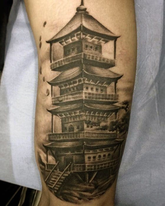 Black and grey forearm tattoo of a detailed multi-tiered Japanese pagoda with soft shadows and subtle background landscape.