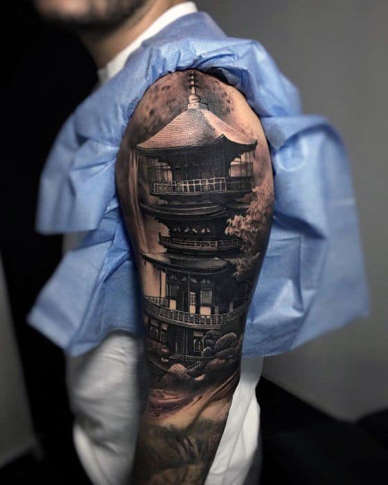 Realistic black and grey upper arm sleeve tattoo of a Japanese pagoda with intricate architectural shading, clouds, and a full moon above.