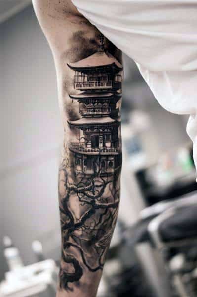 Black and grey full arm tattoo of a Japanese pagoda with misty shading and twisted tree branches wrapping around the design.