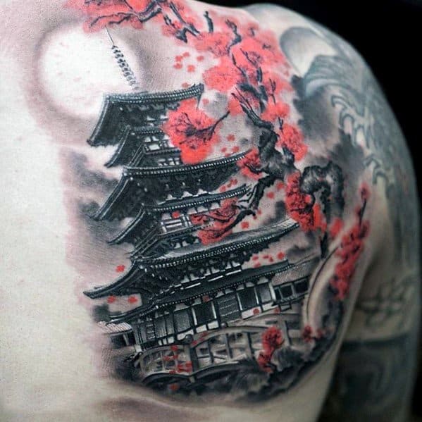 Shoulder tattoo of a Japanese pagoda in black and grey, surrounded by vivid red cherry blossoms and soft background shading for contrast.