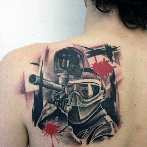 Bold back tattoo of a paintball player in action with a mask and marker gun, accented by red paint splatters for dramatic effect.