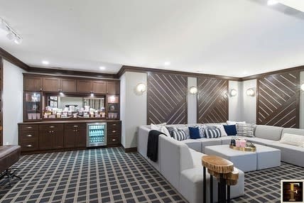 Modern basement living area with large sectional sofa, built-in bar, and geometric wall paneling.