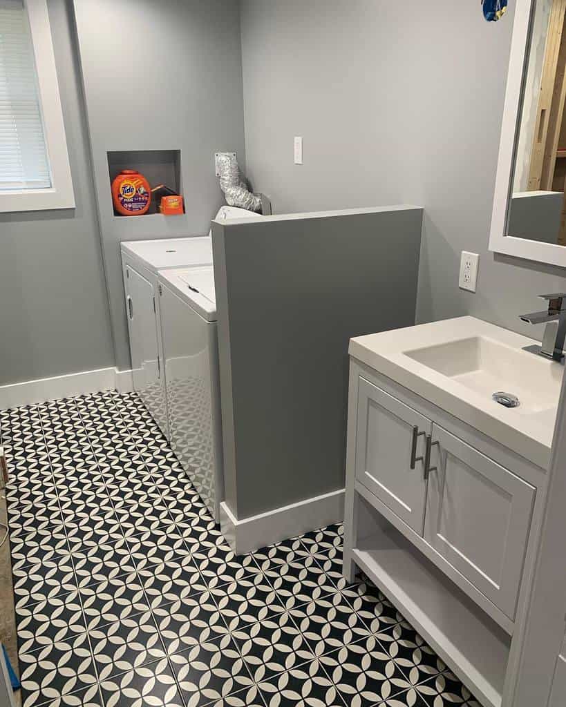 Modern grey laundry room with patterned tile flooring, white washer and dryer, and compact vanity sink.