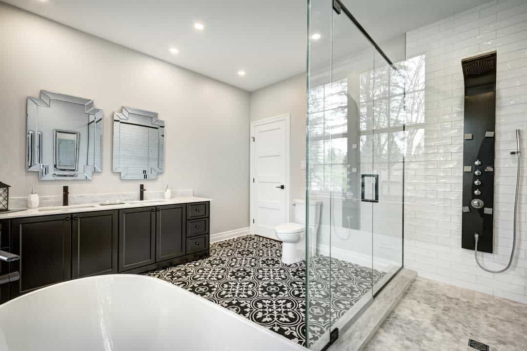 Large modern bathroom with black vanity, patterned tile flooring, glass shower, and freestanding tub.