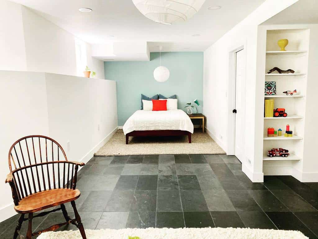 Small children's basement bedroom with built-in shelves, light blue accent wall, and wood furniture.
