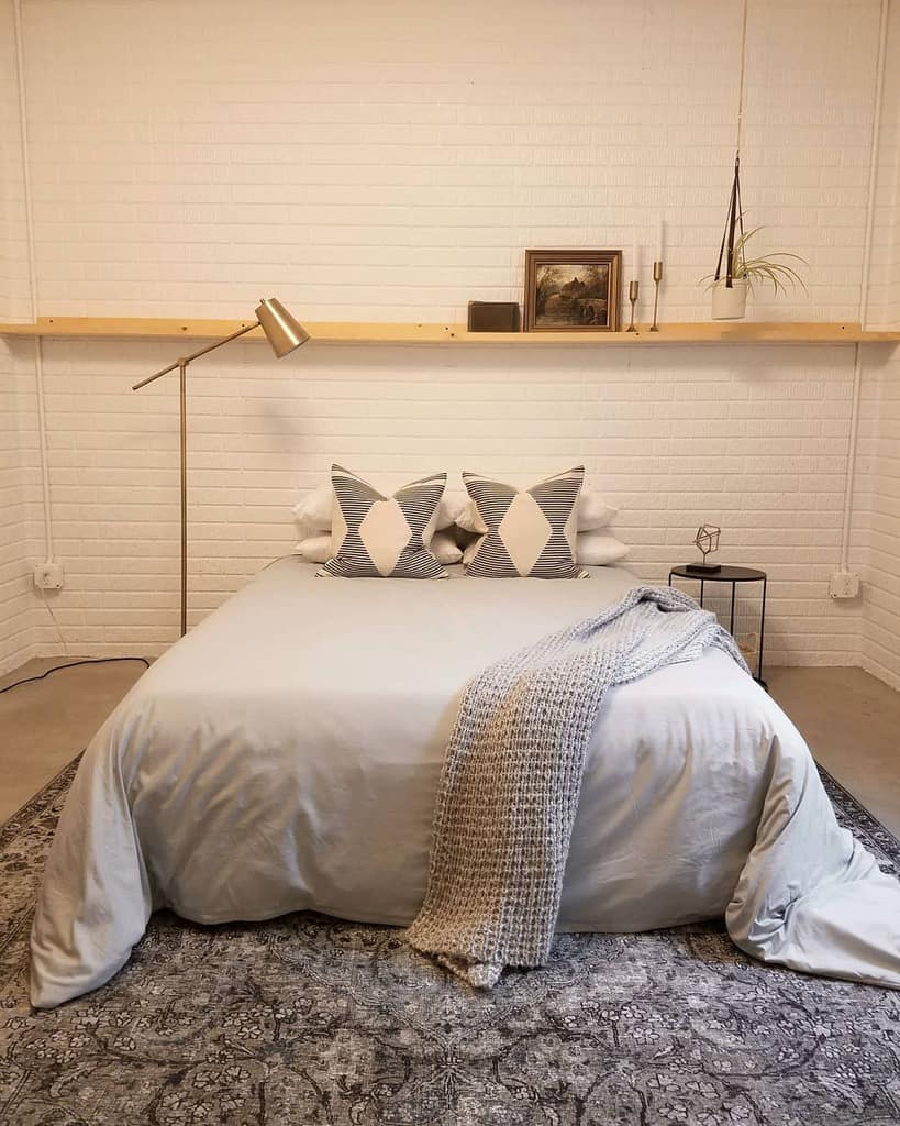 Minimalist bedroom with white brick wall, neutral bedding, and geometric accent pillows.