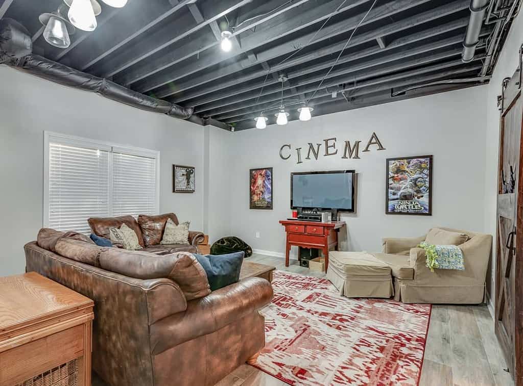 Home cinema room with leather sectional, TV, movie posters, and exposed ceiling beams.