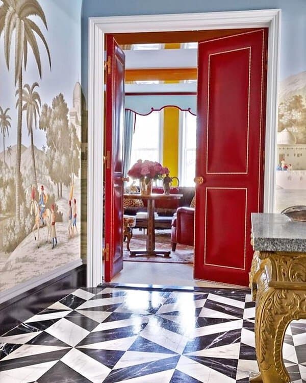 Entry with a black-and-white geometric floor, red doors, gold console, and a scenic wall mural for a dramatic, luxurious statement.