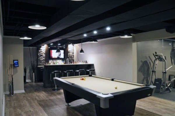 Basement with black exposed ceiling beams, pool table, bar area, and home gym space.