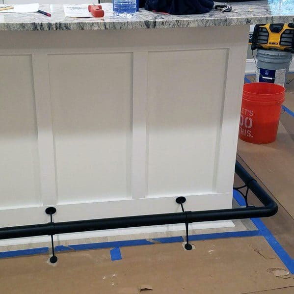 Sleek black pipe foot rail installed on a white bar with a granite countertop in a modern space.