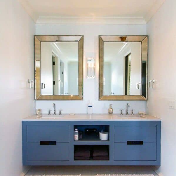Blue double vanity with gold-framed mirrors and open storage compartment.