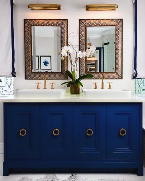 A bold double vanity with blue cabinets paired with gold hardware and matching framed mirrors for an elegant, luxurious look.